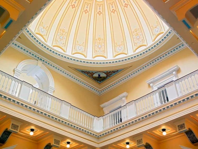 Interior view of the Virginia State Capitol featuring a yellow ornate dome ceiling with decorative elements and elegant balustrades along the upper levels.